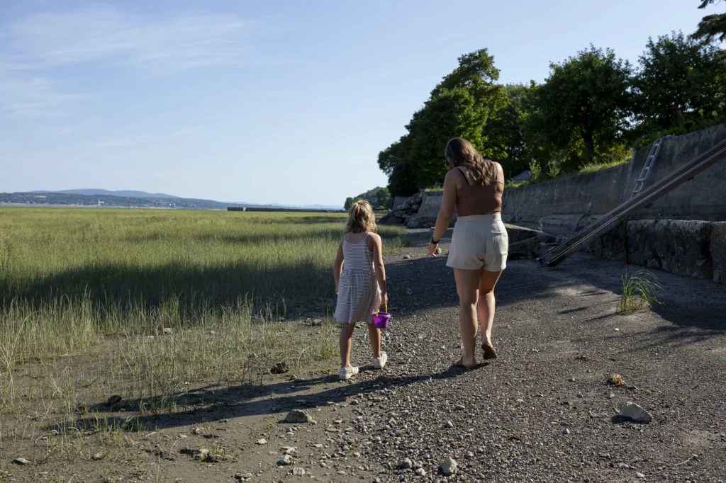 Une femme et une fillette marchant sur un chemin caillouteux près d'un rivage herbeux